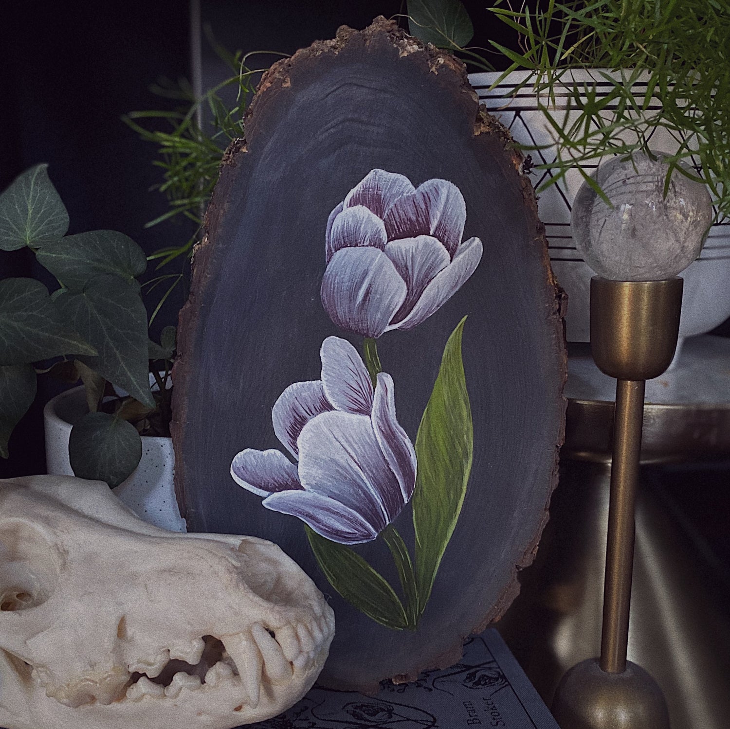 tulip painting on wood arranged next to live plants and skull in gothic aesthetic 